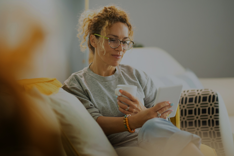 Woman sits on sofa with a mug looking at a tablet