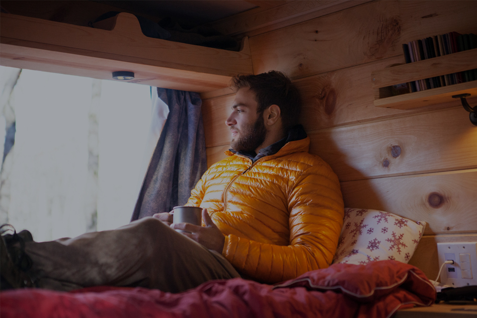 Man drinking tea in a van in camping gear