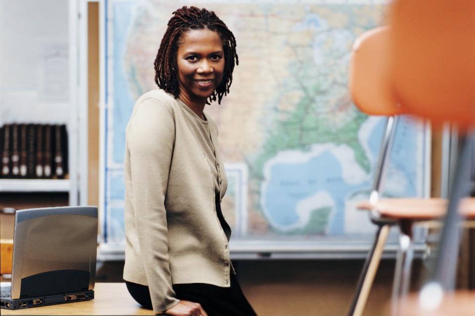 Female teacher leaning on desk in empty classroom