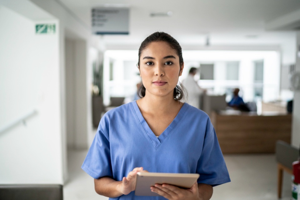 Female student wearing blue scrubs holding an ipad